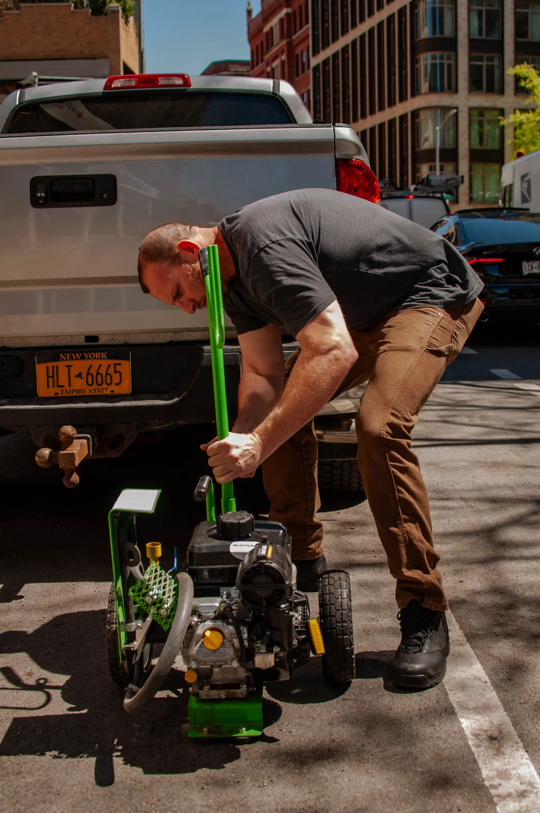 Technician priming a gas-powered sprayer unit at the tailgate of a pickup truck on a city street