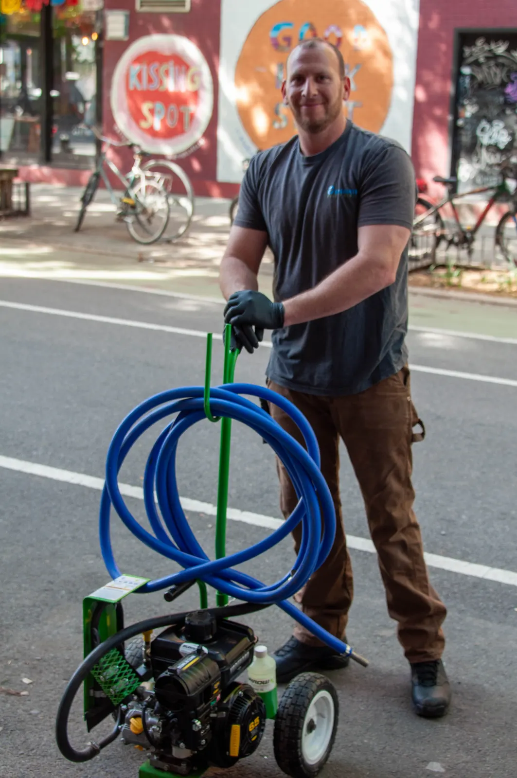 Technician moving a gas-powered sprayer and coiled hose into position on a Brooklyn street